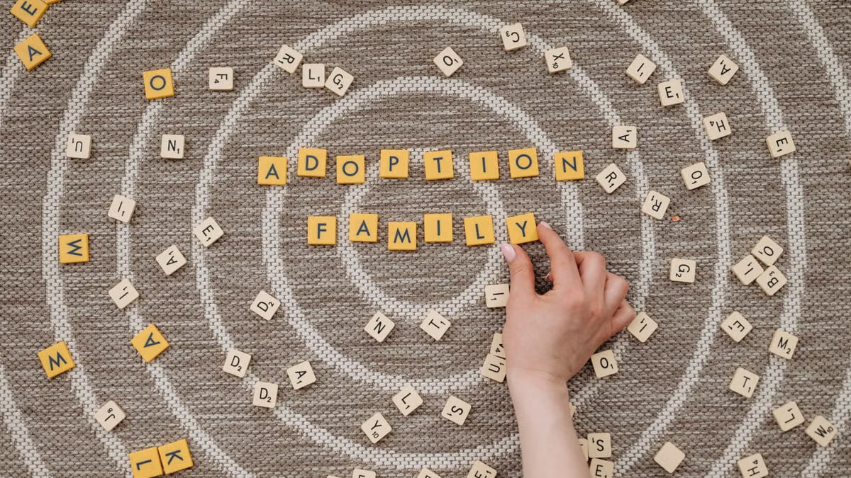 Hand arranging scrabble tiles to spell adoption and family on a circular patterned background.